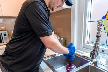 Person unclogging sink with plunger